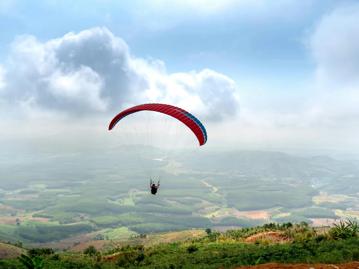 Man Paragliding over Green Grass Field