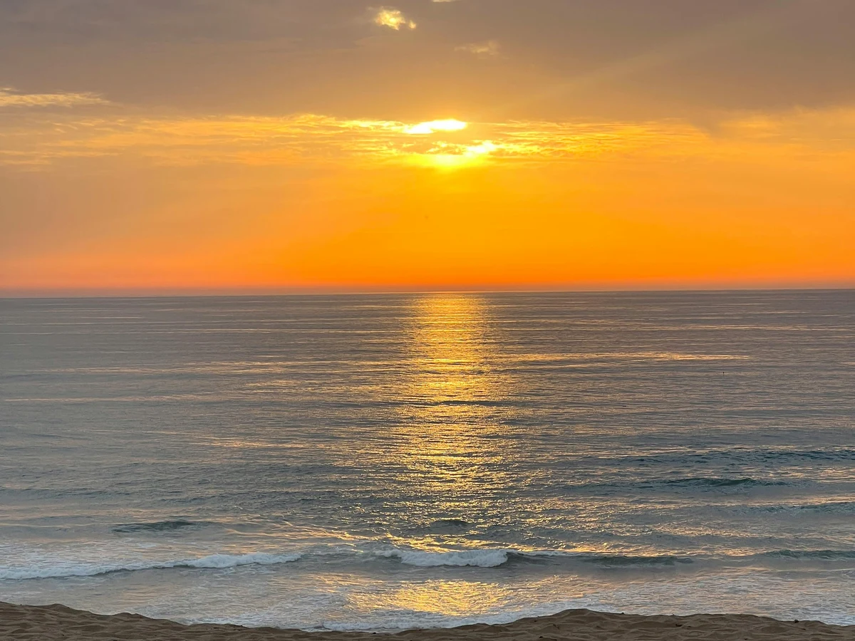 A sunset over the ocean with a person on the beach