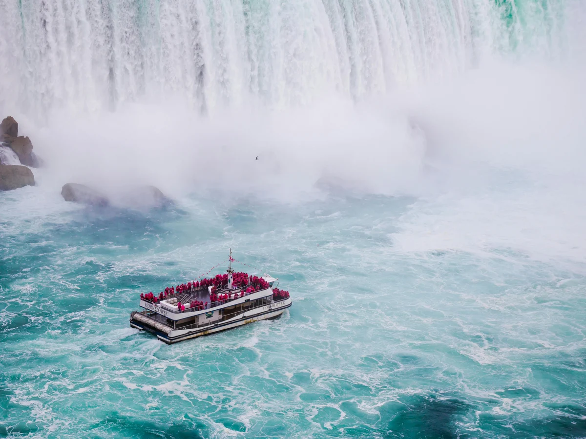 Ship with unrecognizable travelers on river near fast foamy waterfall Canada
